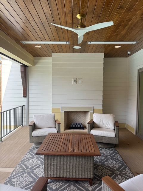 Patio with fireplace, seating, and ceiling fan. Wood ceiling, white walls, and gray rug.