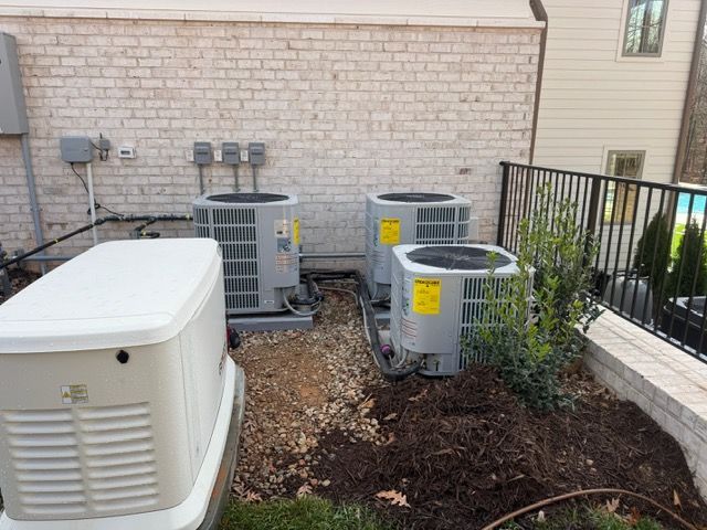 Outdoor air conditioning units and a generator next to a brick wall and a fence.