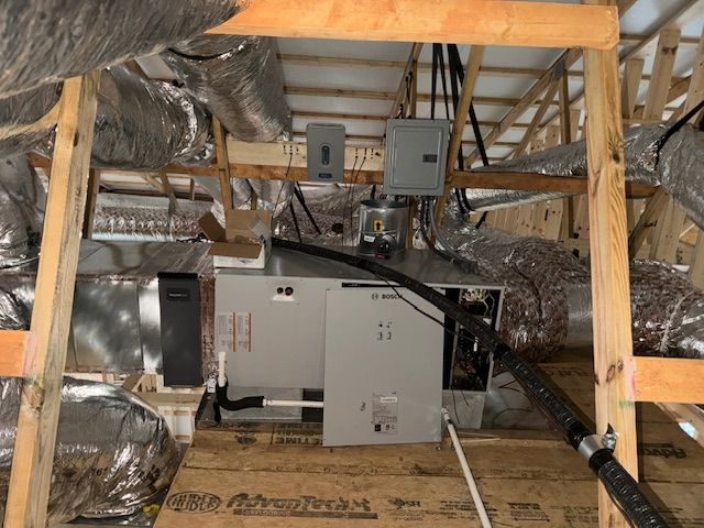 HVAC unit in an attic with ductwork, electrical boxes, and wooden supports.