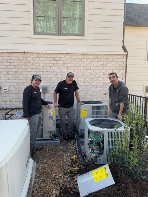 Three people standing near air conditioning units outside a building.