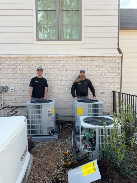 Two technicians standing by three air conditioning units next to a building.