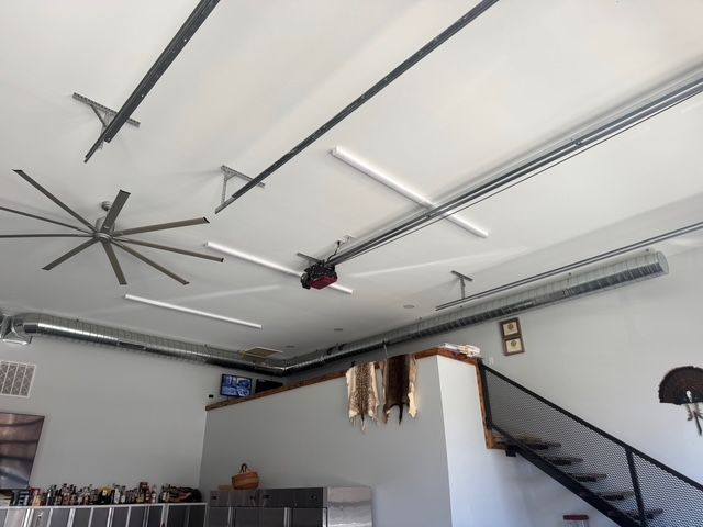 Garage interior with fans, lights, and ductwork on white ceiling. Staircase and wall on the right.