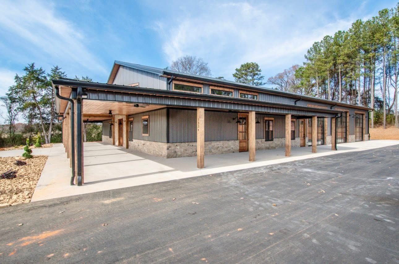 Modern building with a covered walkway and wooden posts, set against a backdrop of trees and a blue sky.