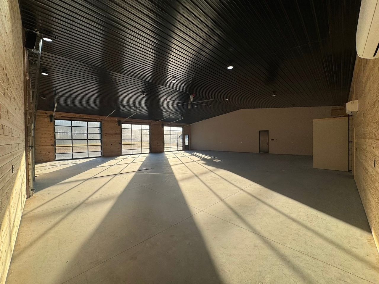 Empty commercial space with curved ceiling, large windows casting shadows on concrete floor.