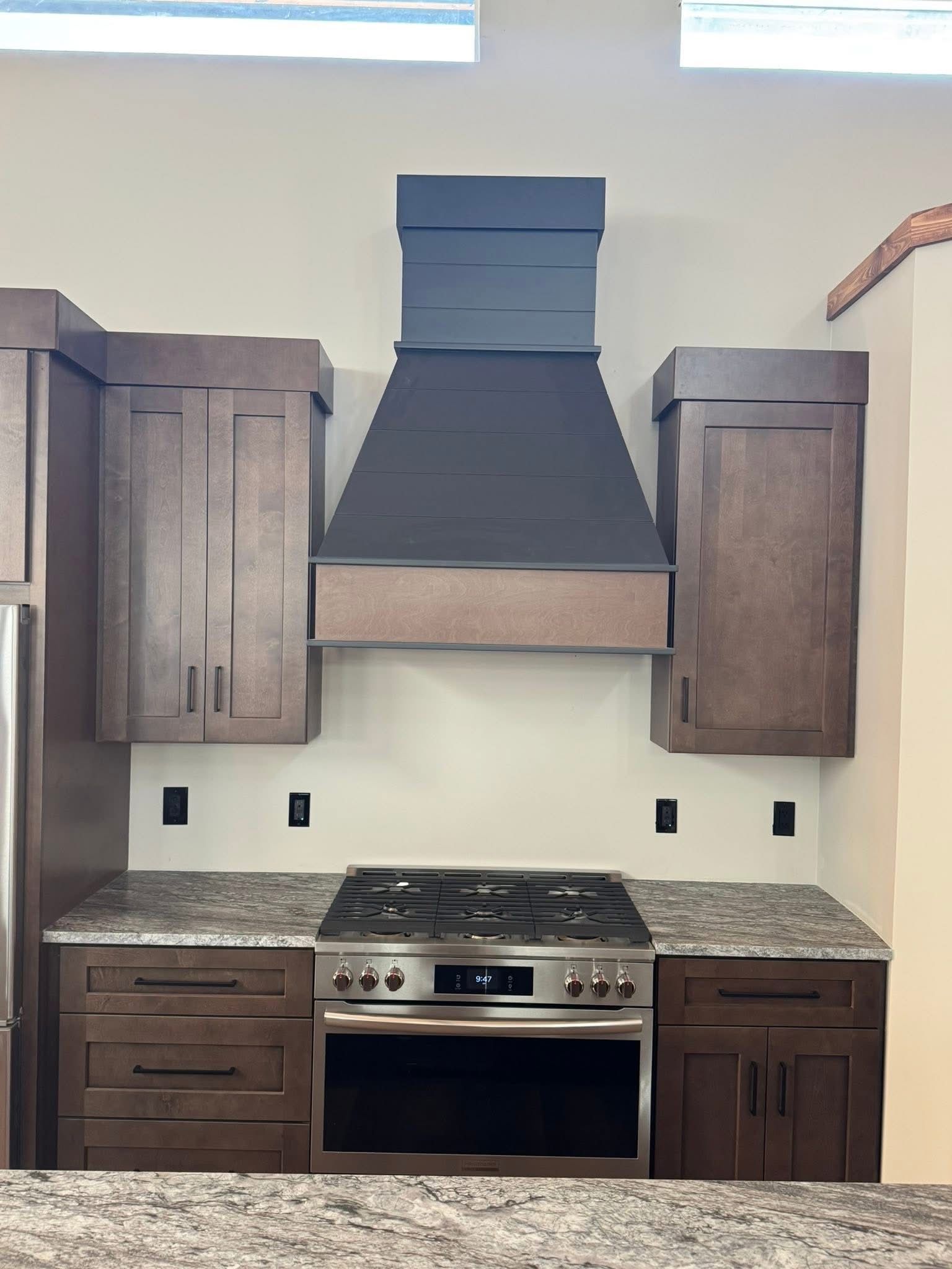 Kitchen with dark cabinets, stainless steel range, granite countertops, and a black range hood.