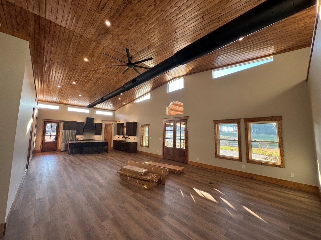 Spacious interior with wood ceiling, dark wood cabinets, and hardwood floors. Windows, a fan, and beams are visible.