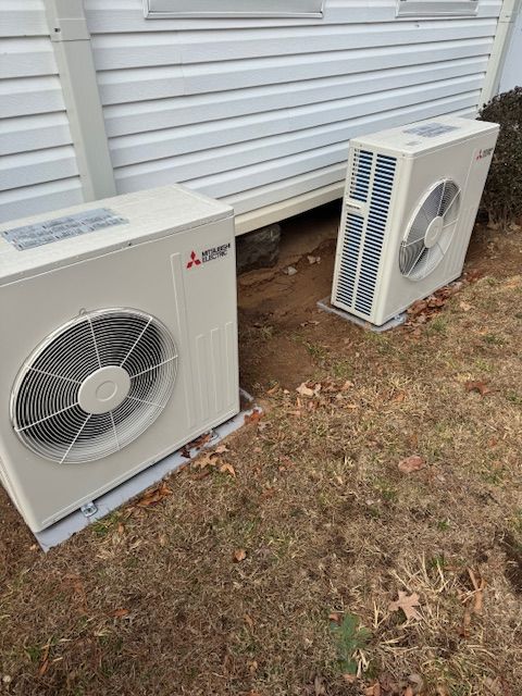Two Mitsubishi heat pump units beside a white building on a grassy lawn.