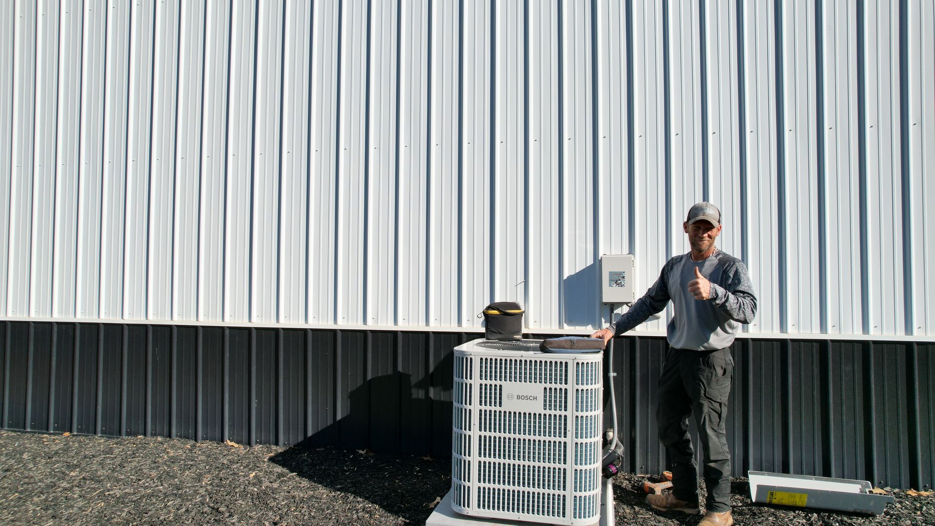 Man next to new air conditioner unit against a white building with dark trim.