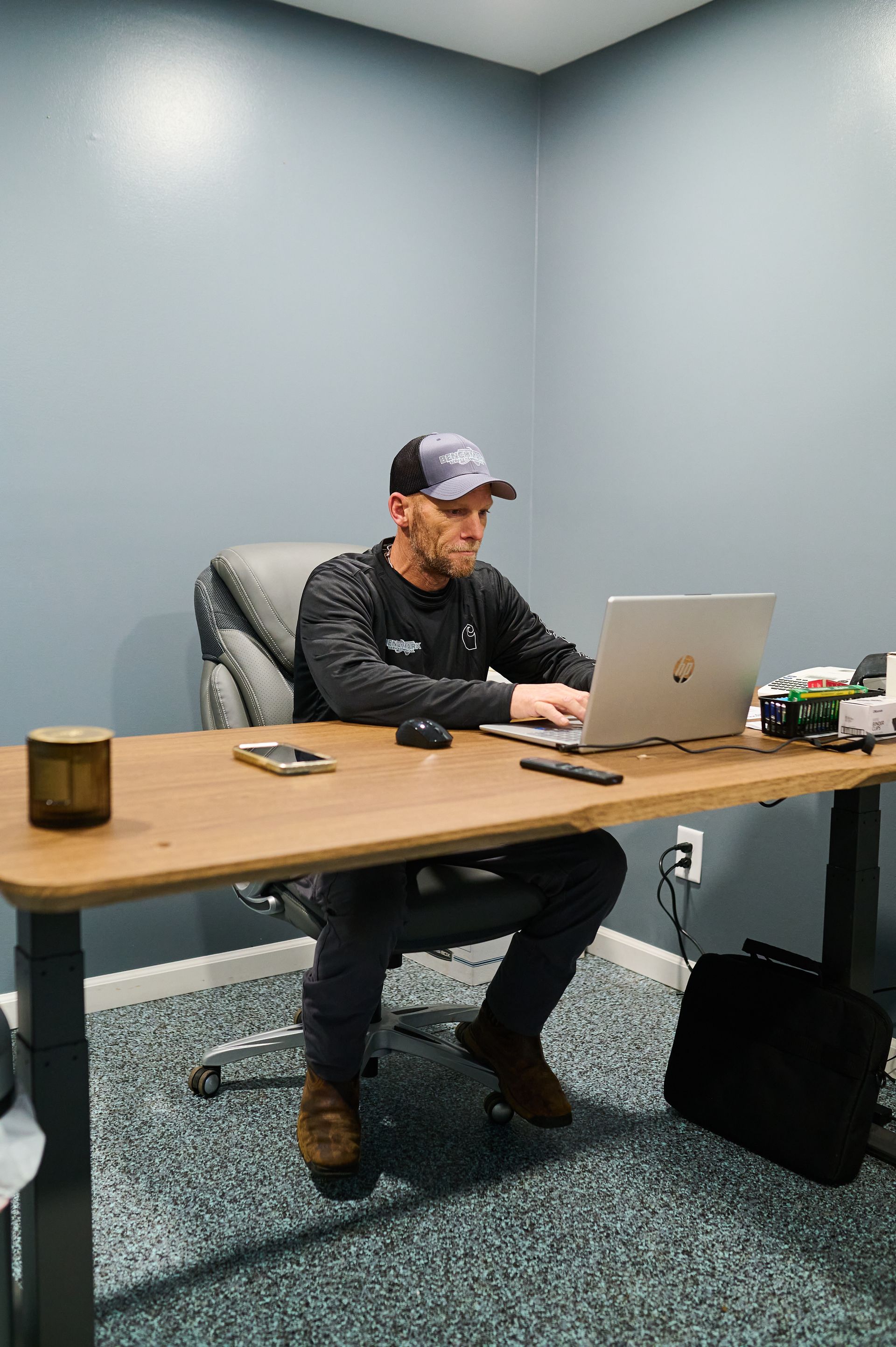 Man seated at a desk, using a laptop in a gray-walled office.