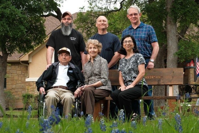 Group photo by a bench, several people in front of a house, surrounded by bluebonnets.