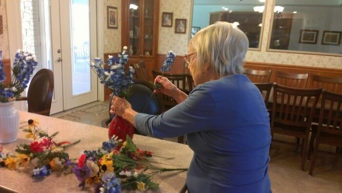 Woman arranges blue and yellow flowers in a vase on a table, indoors.
