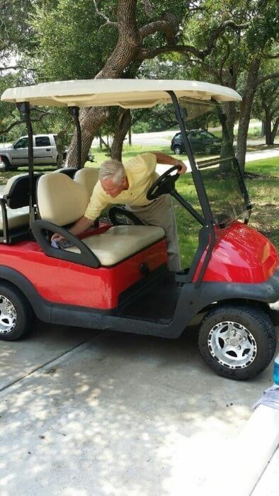 Man in yellow shirt leaning into a red golf cart on a paved driveway.