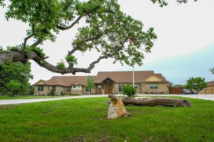 A large, stone-clad building with a sprawling oak tree in front; a grassy yard.