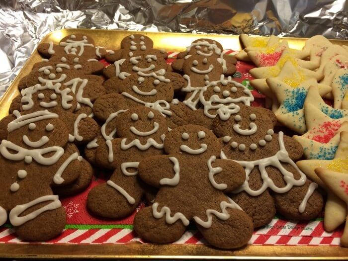 Gingerbread cookies decorated with white icing, and star-shaped cookies with sprinkles, on a tray.