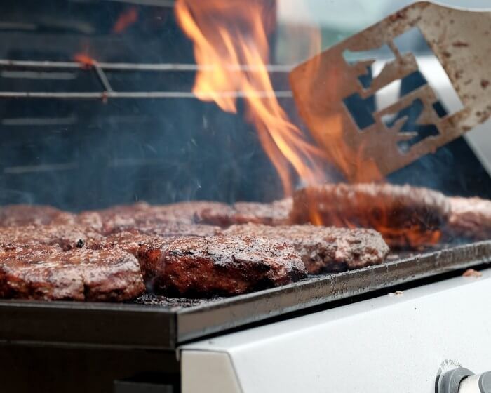 Burgers grilling on a barbecue, flames, spatula.