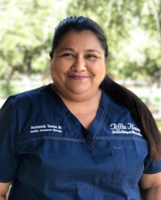 Woman in blue scrubs smiles; outdoor setting; reads