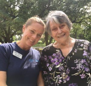 Woman in blue shirt smiles next to older woman with purple floral top, both outdoors.