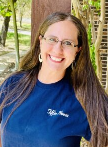 Woman smiling outdoors, wearing glasses and a blue shirt with