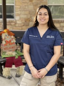 Woman in blue scrubs smiles, standing in front of a bench with a scarecrow.