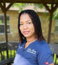 Woman in blue scrubs, smiling outdoors under a gazebo.