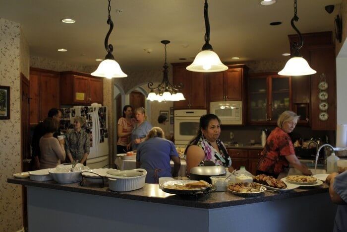 People preparing food in a kitchen with a large island; overhead lights illuminate the space.