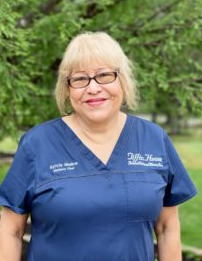 Woman in blue scrubs smiling outdoors. Name tag says