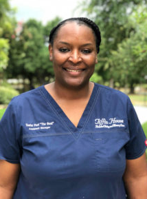 Smiling person wearing a blue scrub top, outdoors. Text on the scrub reads “Telfair House Resident & Employee Services.”