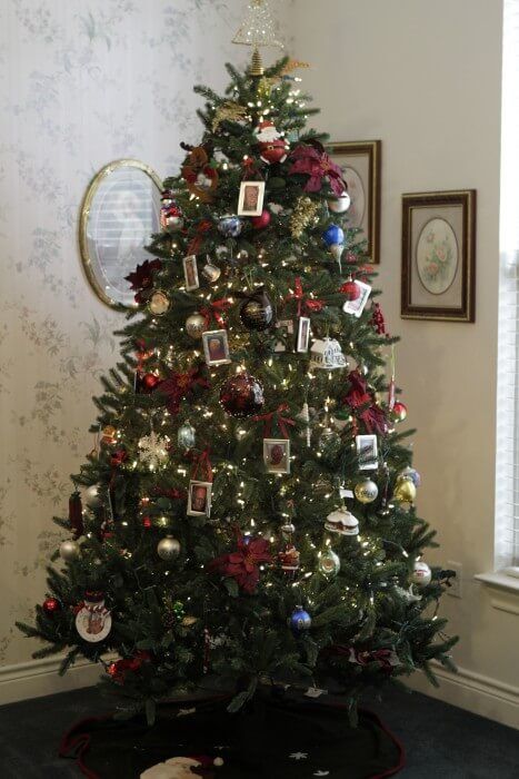 Christmas tree with ornaments and lights in a corner, with framed pictures and a mirror nearby.