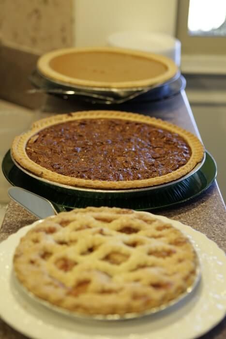 Three pies: pumpkin, pecan, and apple lattice-top, on a counter.