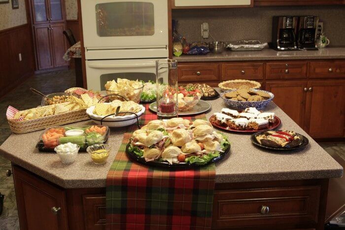 Kitchen island spread with various appetizers, including chips, sandwiches, and desserts, ready for a gathering.