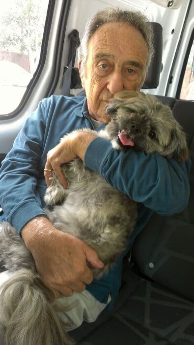 Man holding a fluffy, gray and white dog in a car. Dog has tongue out.