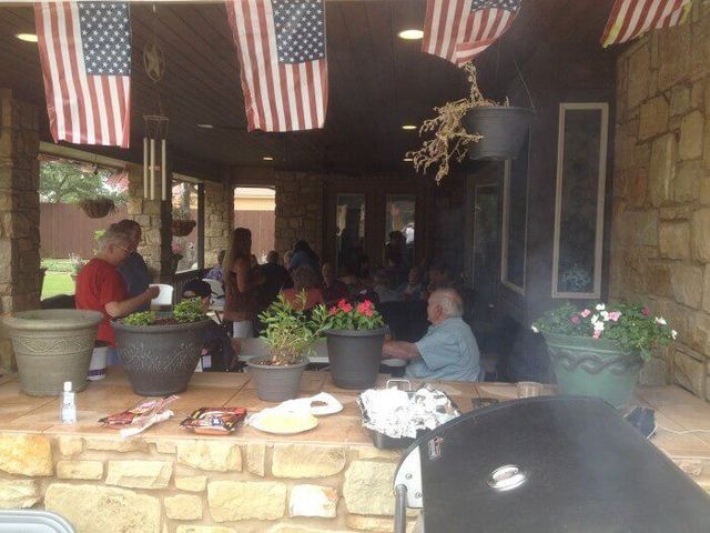 Patio gathering with American flags, people, food, and potted plants.