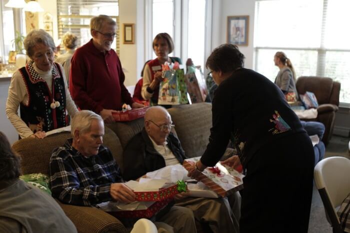 People gathered around a couch, opening gifts at a holiday celebration, indoors.