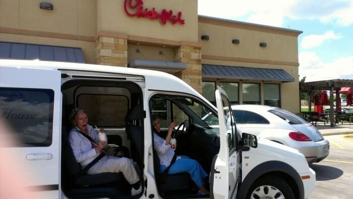Two people excitedly seated in a white van outside a Chick-fil-A. One arm raised.
