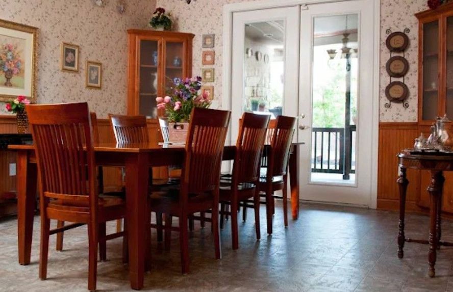 Dining room with wooden table, chairs, cabinets, flowers, and doors leading to a porch.