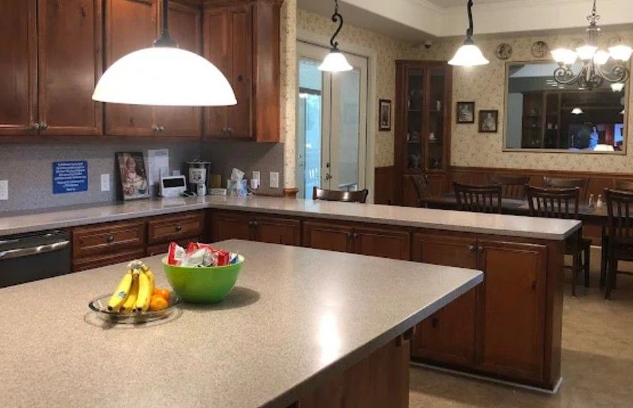 Kitchen with brown cabinets, light countertops, and fruit bowl on the island. Dining area visible.