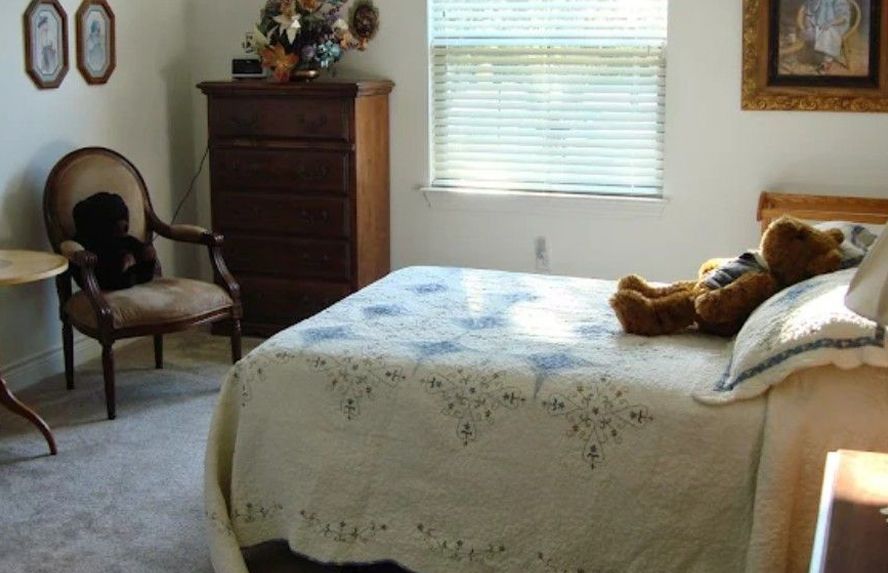 Bedroom with bed, dresser, chair, and window. Teddy bear on bed.