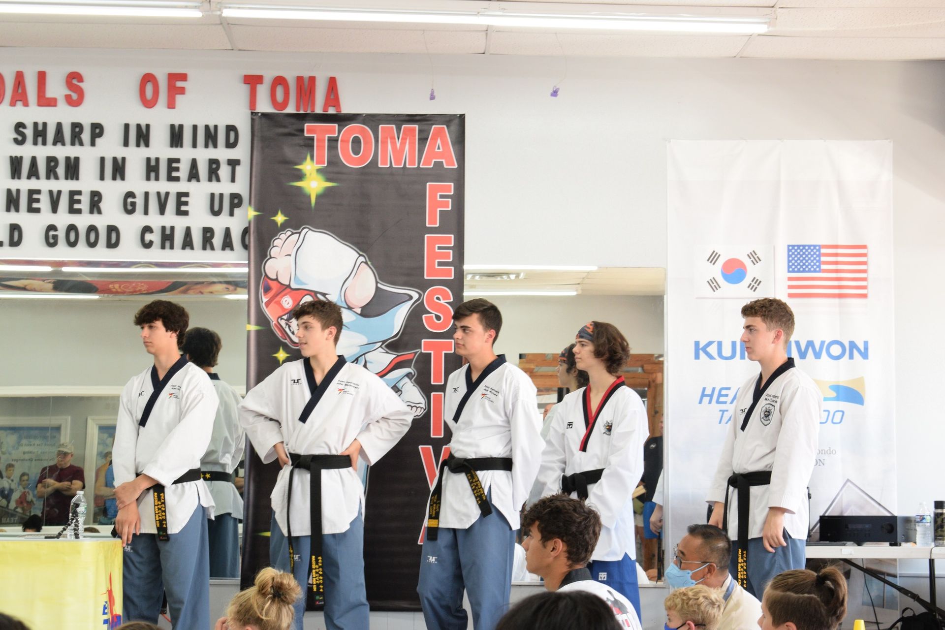 People in martial arts uniforms at a festival. Flags of South Korea and the USA are in the background.