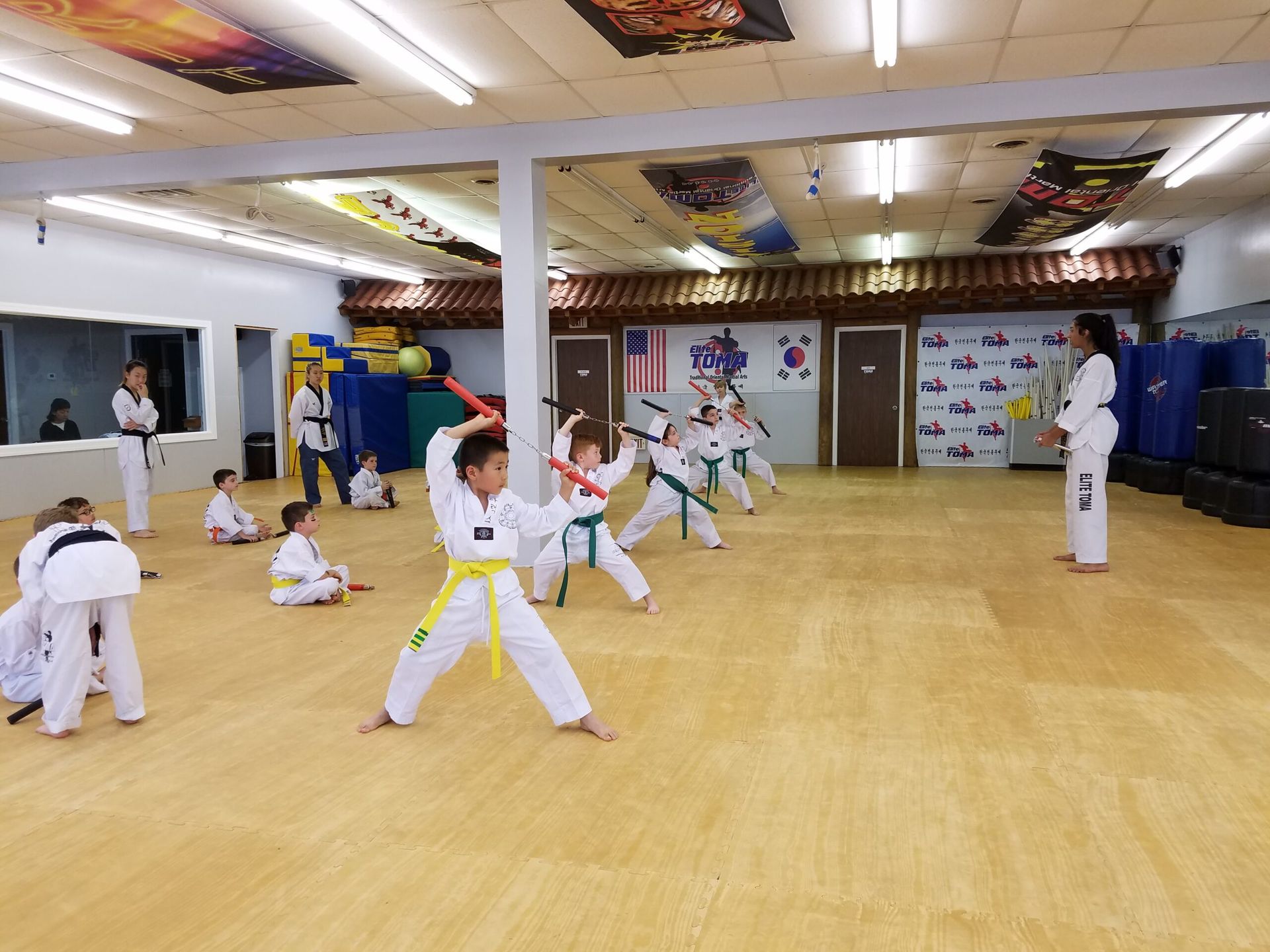 Kids practicing martial arts with nunchucks in a dojo; yellow and green belts.