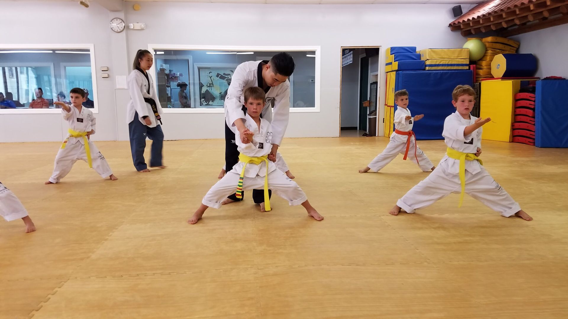 Children in yellow belts practice martial arts under instructor's guidance in a dojo.