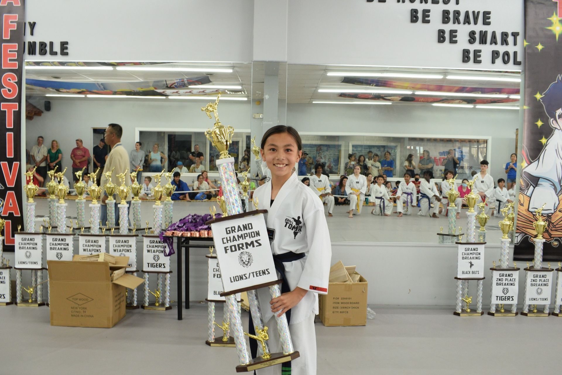 Girl in karate uniform holding trophy in a martial arts studio, many trophies in the background.