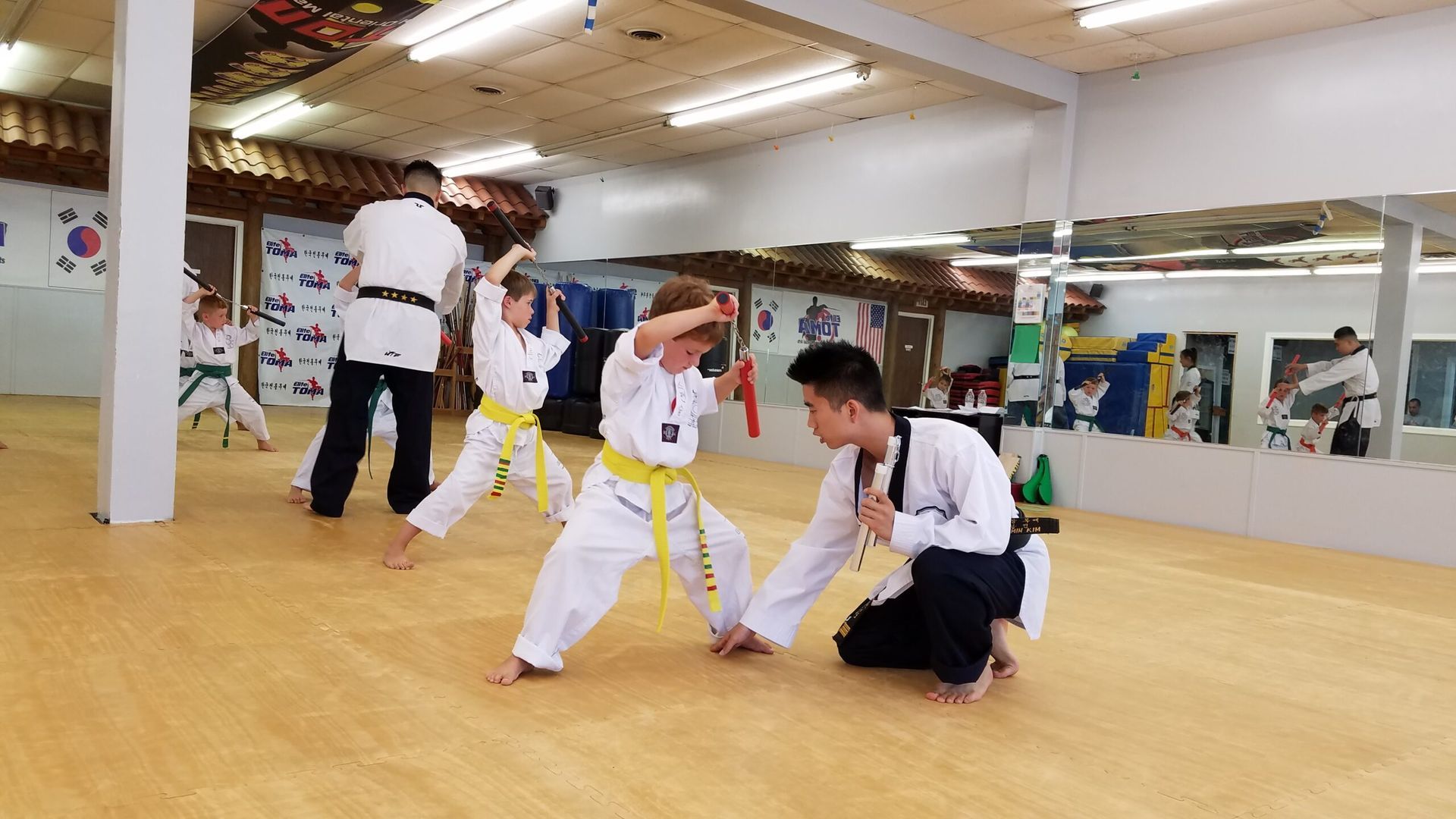 Children in white uniforms with yellow belts practice martial arts under the guidance of instructors in a dojo.