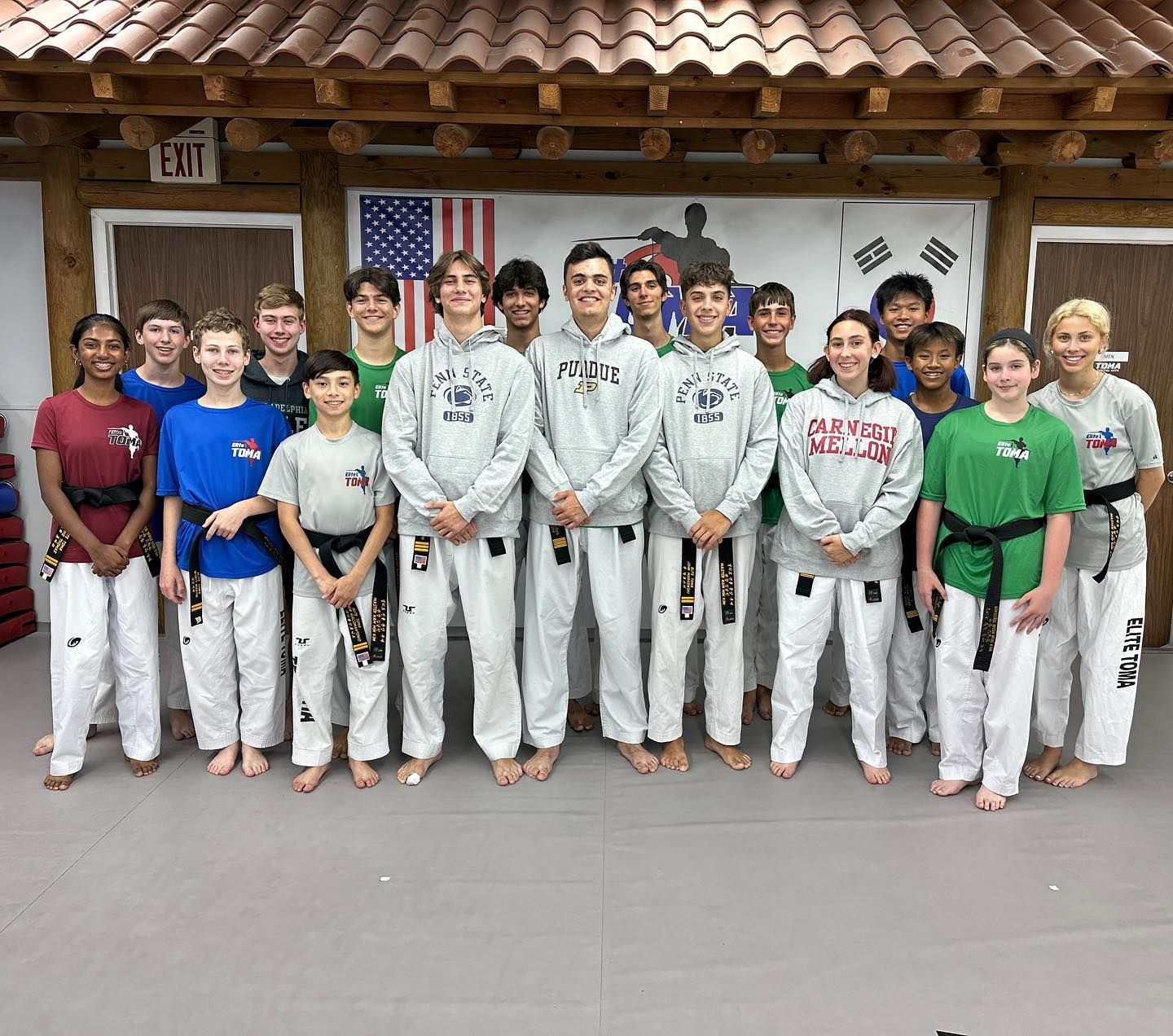 Group of people in martial arts uniforms, posed indoors in front of flags.