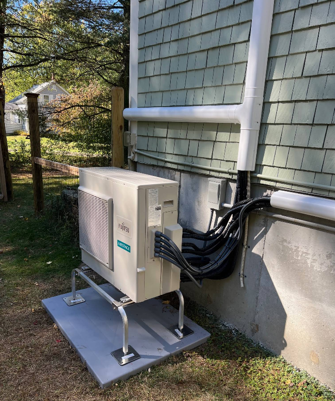 Outdoor HVAC unit beside a house, with white conduit and black cables on a concrete pad.