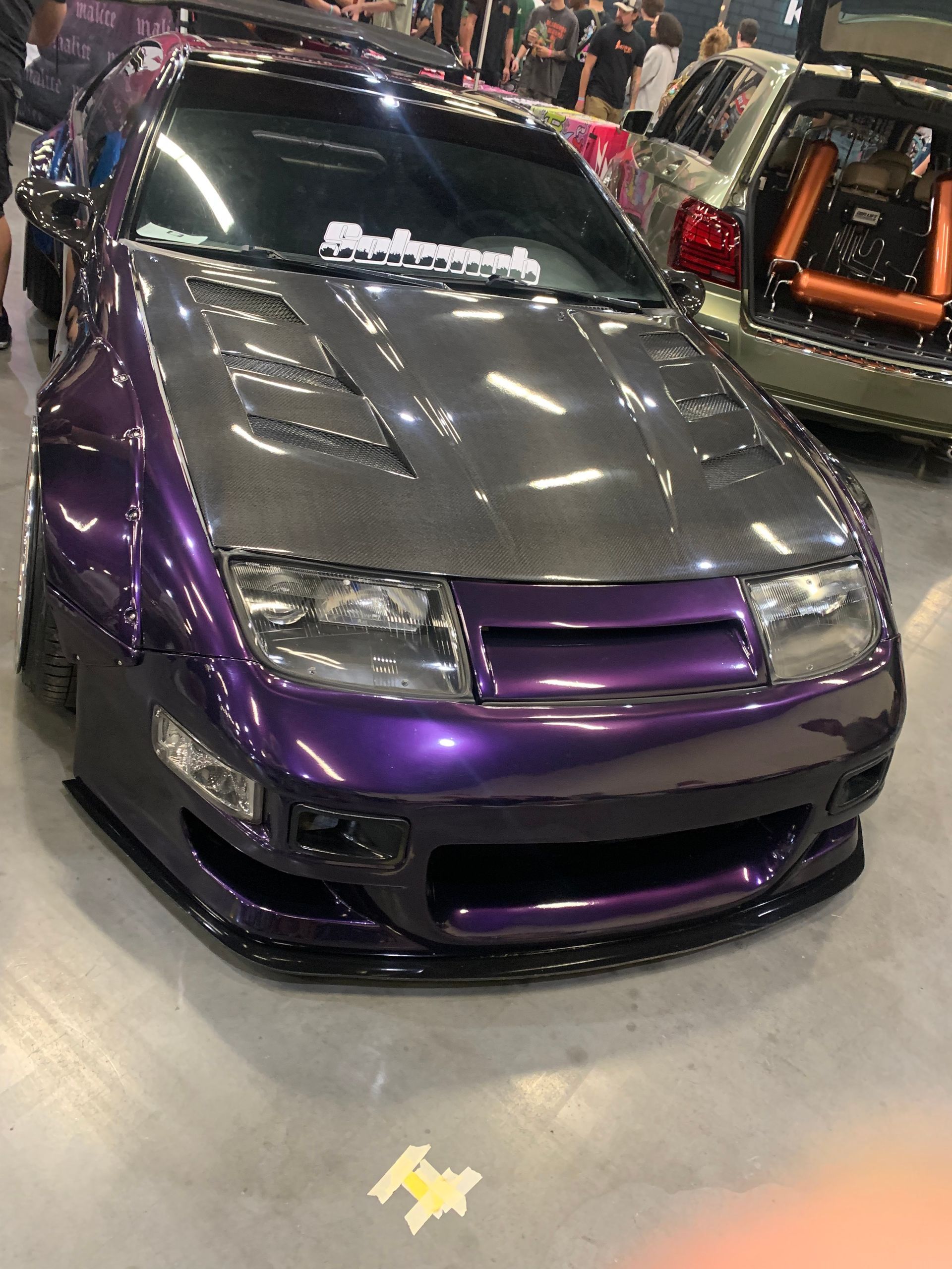 A modified purple Nissan 300ZX with a carbon fiber hood and widebody kit on display at an indoor car show.