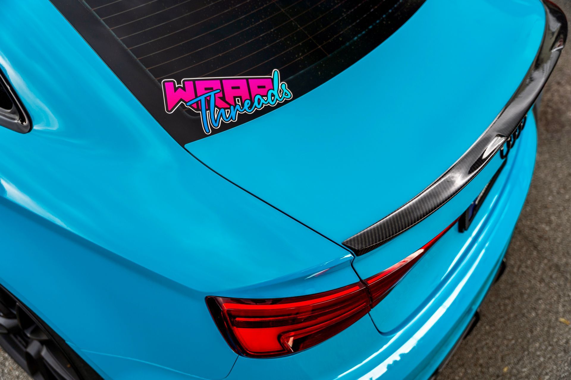 A bright cyan car with a carbon fiber spoiler and a 