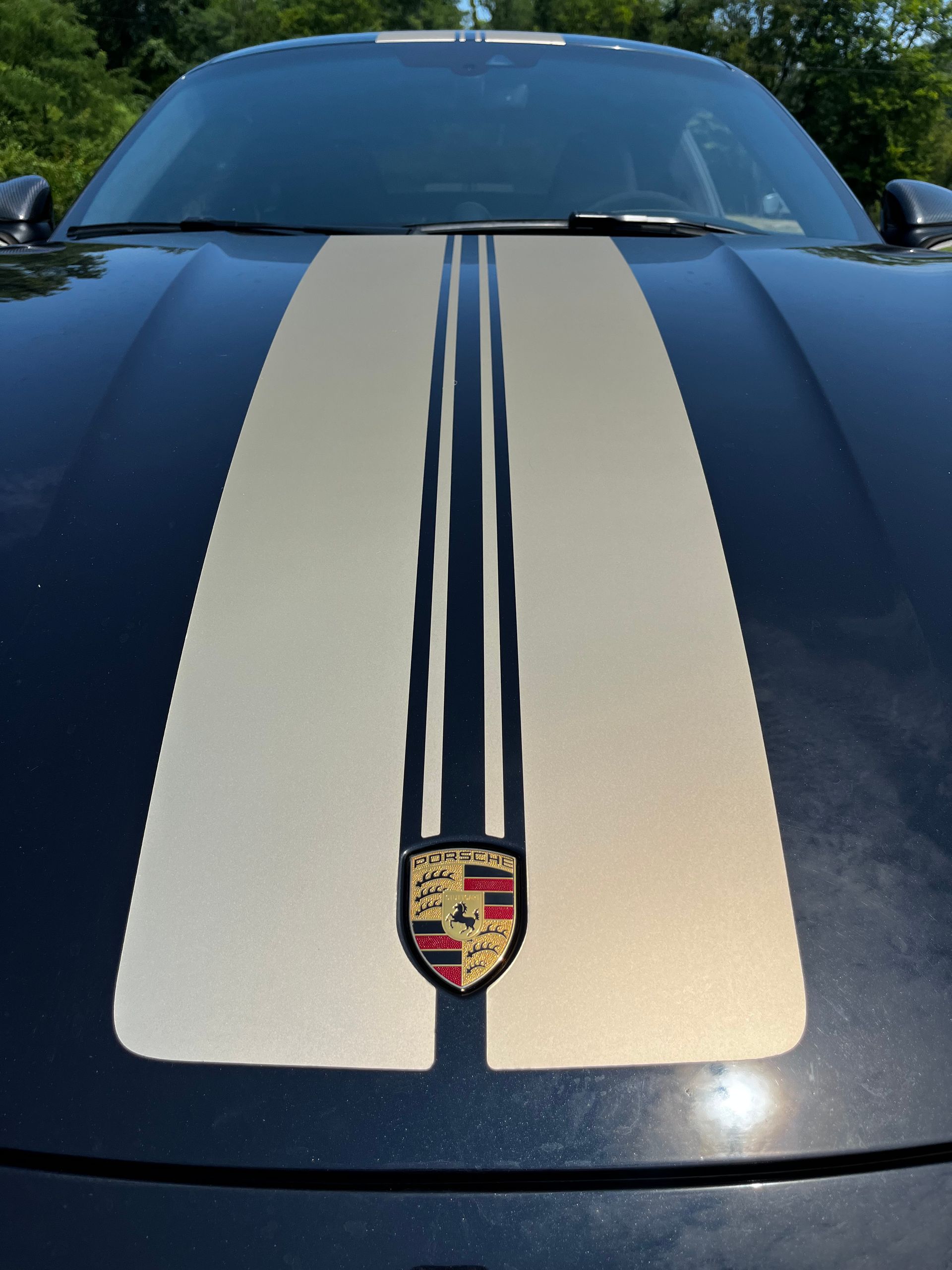 A black Porsche hood featuring a wide, metallic gold racing stripe with a thin black pinstripe design down the center.