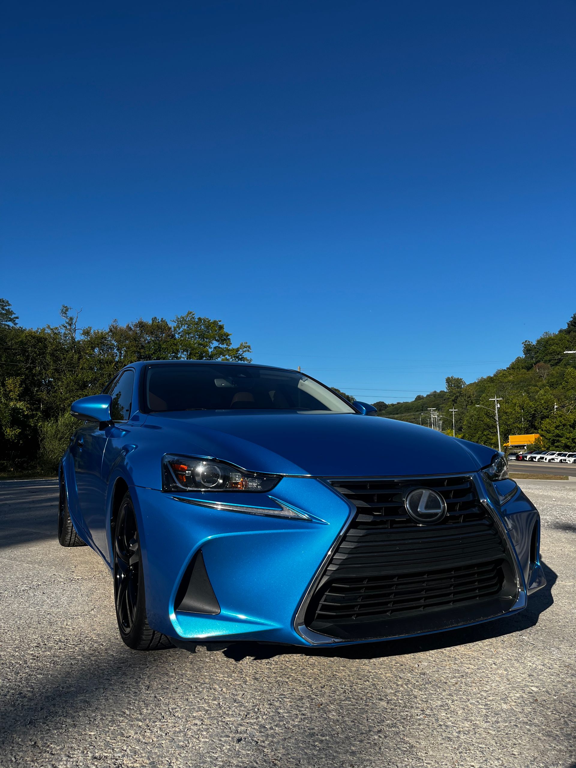 A vibrant blue Lexus sedan parked on a gravel lot under a clear blue sky.