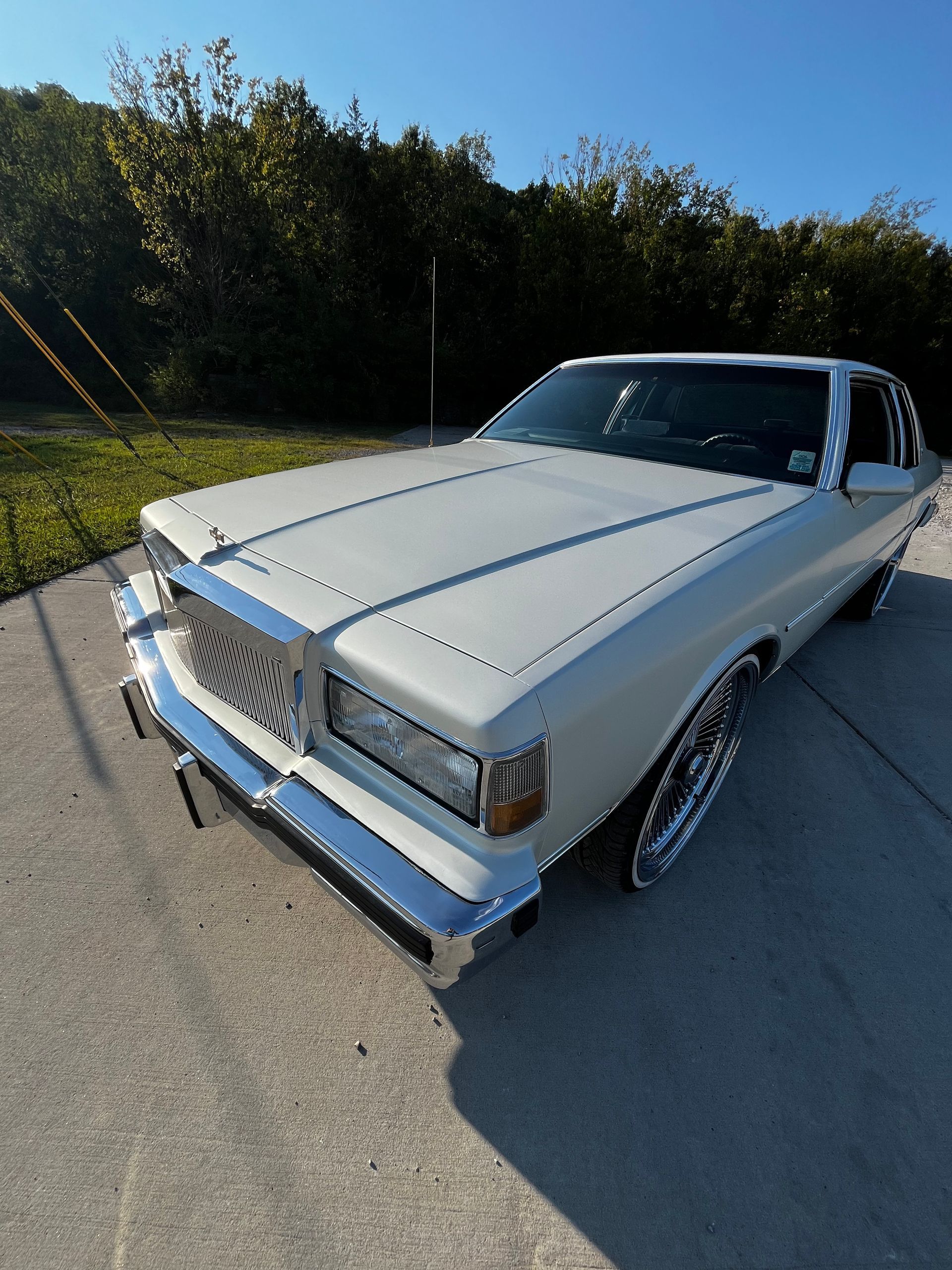 A high-angle shot of a white vintage luxury car with chrome trim and oversized custom wheels, parked on a paved lot.