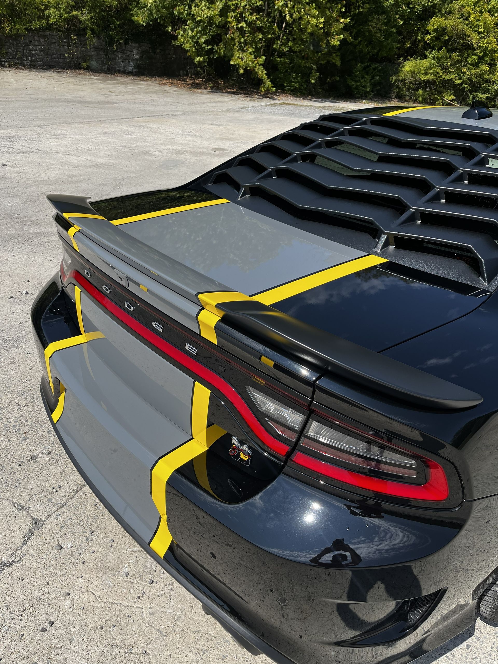 Rear view of a black Dodge Charger with a gray racing stripe, yellow accents, and rear window louvers.